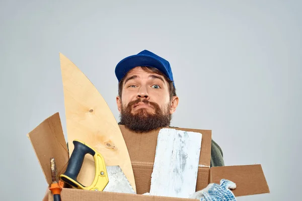 Hombre en uniforme de trabajo con caja en las manos herramientas estilo de vida fondo claro — Foto de Stock