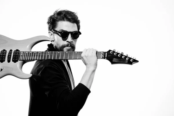 Ein Mann hält eine Gitarre in der Hand schwarze Lederjacke dunkle Brille Musikperformance hellen Hintergrund — Stockfoto
