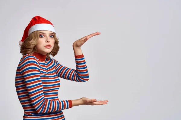 Noel şapkalı ve çizgili kazaklı mutlu bir kadın yılbaşı tatili için elleriyle el kol hareketi yapıyor. — Stok fotoğraf
