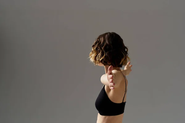 Una donna snella in leggings neri su uno sfondo grigio gesti con le mani ginnastica sport — Foto Stock