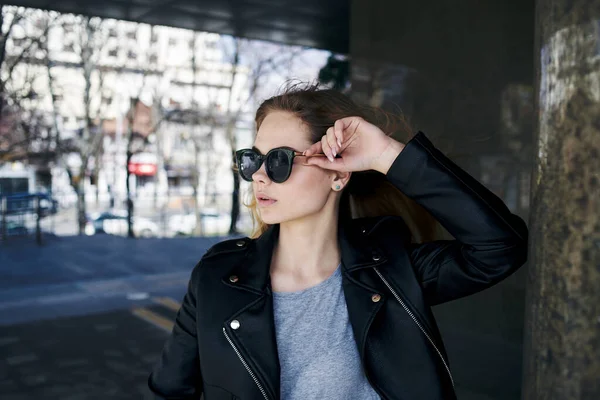 Модная женщина в солнцезащитных очках идет по улице возле здания — стоковое фото