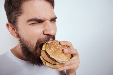 Beyaz bir tişörtle arka planda hamburger yiyen bir adam yakın çekim açlık ve fast food manzarası izledi.
