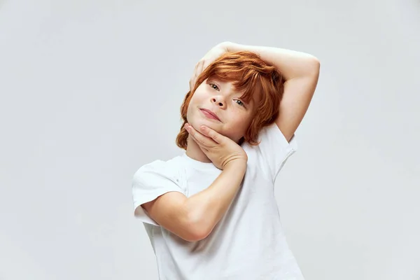 Alegre vermelho de cabelos menino segurando sua cabeça sorrindo branco t-shirt recortada vista — Fotografia de Stock