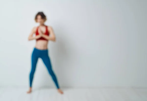 Жінка робить йогу в світлій кімнаті і синіх легінсах червоний бак зверху — стокове фото