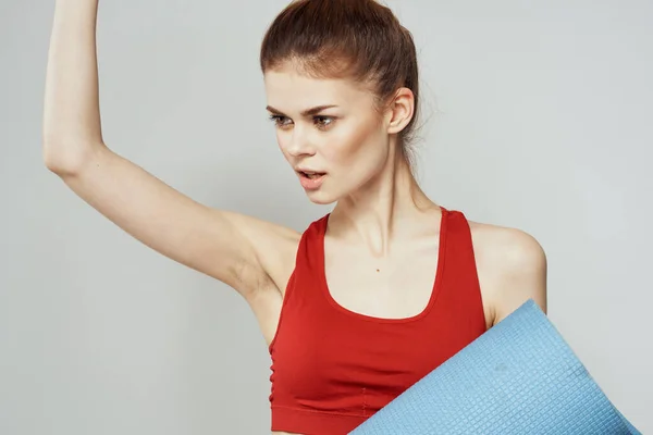 Mujer sostiene en la mano una alfombra para fitness deporte figura delgada ejercicios fondo claro — Foto de Stock