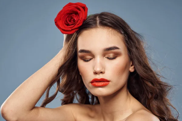 Portrait de femme avec rose rouge près du visage sur fond gris et maquillage cheveux bouclés — Photo