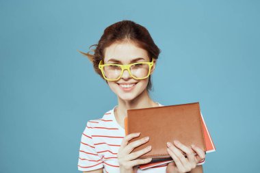 Okul müdürünün mavi arka planında not defterleri ve gözlüklü saç stili olan kız öğrenci.