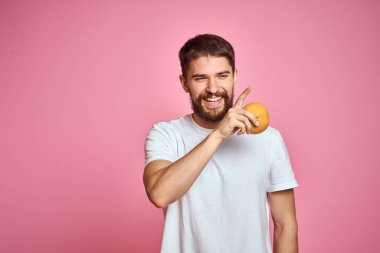 Pembe arka planda, beyaz tişörtlü, turuncu elbiseli genç bir adam. Model ellerle el kol hareketi yapmak eğlenceli.