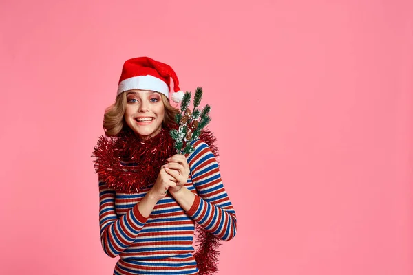 Kobieta z gałęziami choinki w dłoniach czerwony świecidełko i świąteczny kapelusz różowy tło przycięte widok — Zdjęcie stockowe