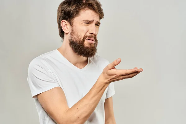 Ein Mann in einem weißen T-Shirt mit einem Bart Emotionen missfallen Gesichtsausdruck Licht Hintergrund — Stockfoto