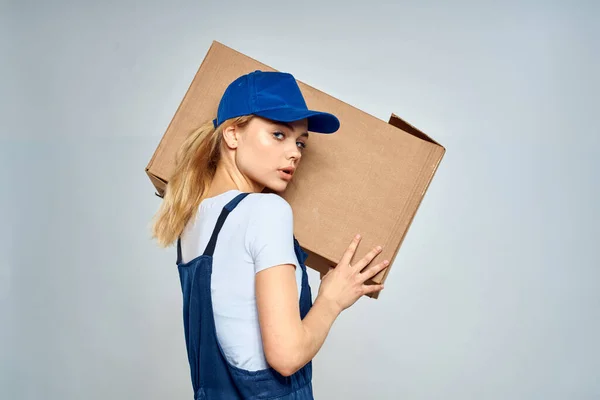 Kobieta w roboczym mundurku z pudełkiem w rękach dostawcy usługi dostawy lekkie tło — Zdjęcie stockowe
