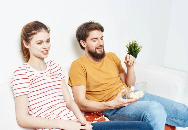 Um homem e uma mulher em um sofá branco Em um quarto brilhante um prato de pipoca e amigos uma flor em um pote — Fotografia de Stock