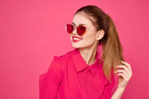 Radosna kobieta w okularach przeciwsłonecznych dotykająca włosów rękami i różową koszulą — Zdjęcie stockowe