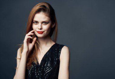 Siyah elbiseli, gri arka planda kızıl saçlı bir kadın elleriyle işaret ediyor.