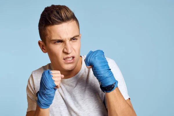 Hombre deportivo en guantes de boxeo azul y camiseta sobre fondo azul practicando golpes vista recortada — Foto de Stock