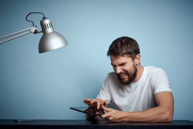 Tabletli adam kapalı masa ve lambalı ofis çalışanı mavi arka plan