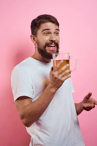 Homme barbu avec une tasse de bière Sur un fond rose émotions amusantes vue recadrée d'un T-shirt blanc ivre — Photo