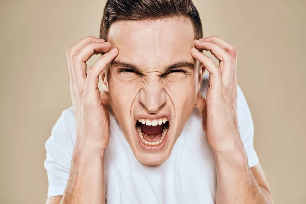 Man with displeased facial expression emotions white t-shirt gestures with hands beige background