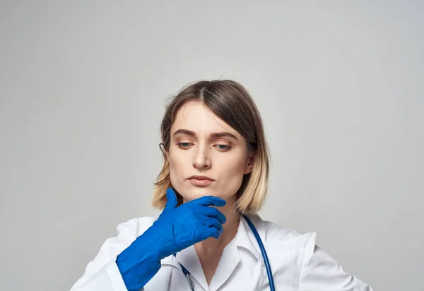 Mujer emotiva con guantes médicos azules toca su cabeza con las manos sobre un fondo claro — Foto de Stock