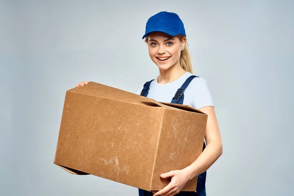 En kvinna i arbetsuniform med en låda i händerna på en leverans tjänst leverans ljus bakgrund — Stockfoto