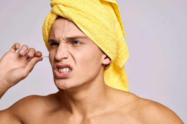 Un uomo con un asciugamano giallo sulla testa e bastoni per le orecchie cosmetologia della pelle pulita — Foto Stock