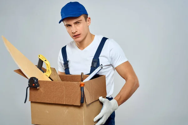 Uomo in uniforme di lavoro con una scatola nelle sue mani strumenti caricatore consegna luce sfondo — Foto Stock