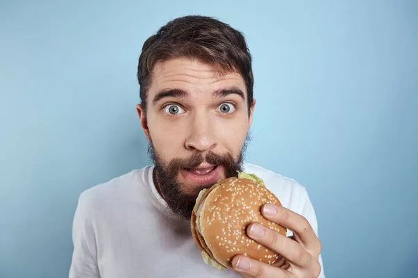 Emocjonalny człowiek hamburger fast food dieta jedzenie zbliżenie niebieskie tło — Zdjęcie stockowe