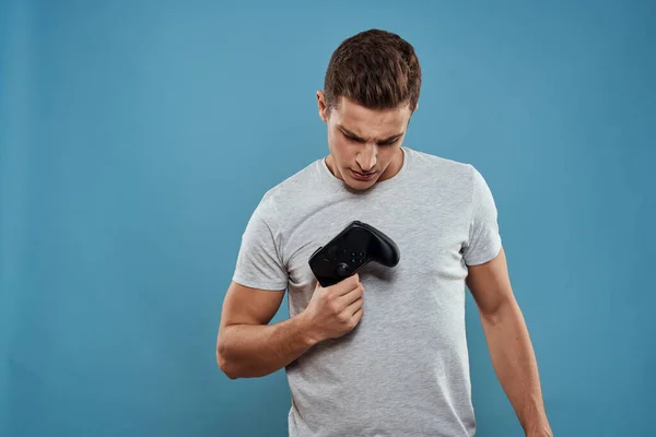 Ένας άντρας με ένα χειριστήριο στα χέρια του τεχνολογία ψυχαγωγίας βιντεοπαιχνίδια μπλε φόντο λευκό μπλουζάκι — Φωτογραφία Αρχείου