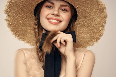 Hasır şapkalı, siyah kurdeleli ve arka planda açık bir elbise giyen hoş bir kız. Romantik bir model.