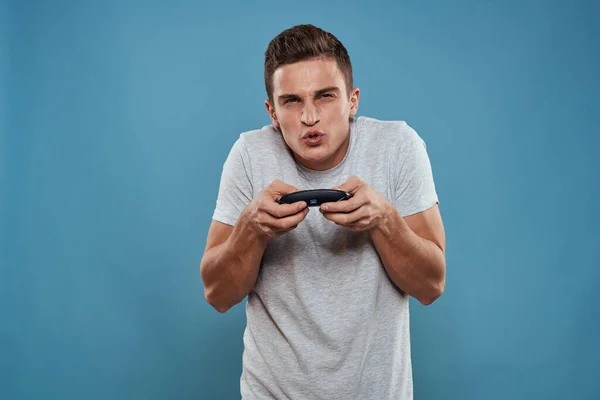 Un hombre con un joystick en sus manos entretenimiento tecnología de ocio videojuegos fondo azul camiseta blanca —  Fotos de Stock