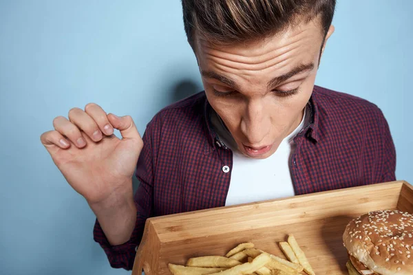 Man met houten pallet fast food frites hamburger honger dieet voedsel blauwe achtergrond — Stockfoto