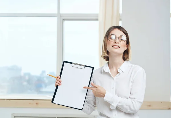 Une femme tient un dossier avec une feuille de papier blanche et une fenêtre en arrière-plan — Photo