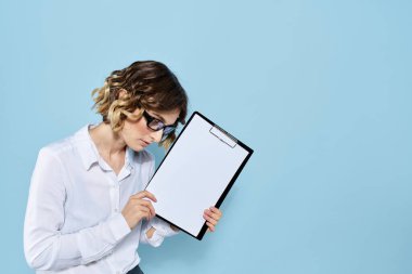 Mavi arka planda bir klasörde evrakları olan ve yüzünde açık renk gözlüklü bir iş kadını.