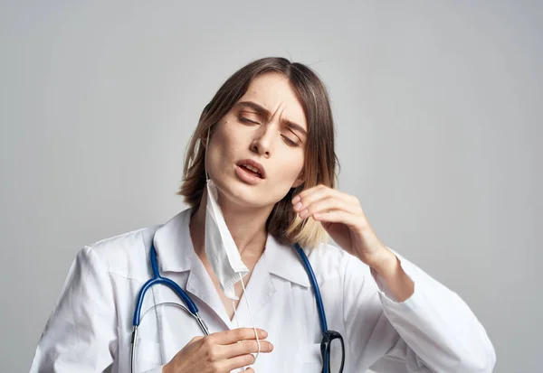 Médico profesional con un estetoscopio y en un vestido médico con una máscara médica de fondo claro —  Fotos de Stock