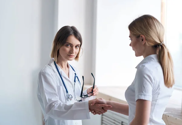 Een vrouwelijke arts in een medisch gewaad luistert naar de problemen van een patiënt in een wit T-shirt — Stockfoto