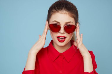 Mavi arka plandaki kırmızı gömlekli kadın yüz ve güneş gözlüklü kırmızı dudak makyajı modeli ile el ele tutuşuyor.
