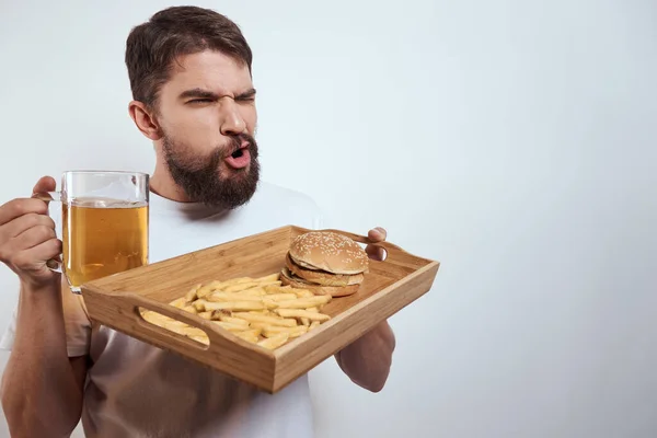 Homem com bandeja de madeira caneca de cerveja batatas fritas e hambúrguer fast food calorias modelo branco t-shirt — Fotografia de Stock