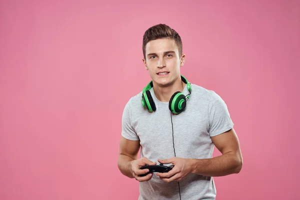 Un hombre con un joystick en sus manos auriculares jugando juegos de entretenimiento estilo de vida camiseta blanca fondo rosa —  Fotos de Stock