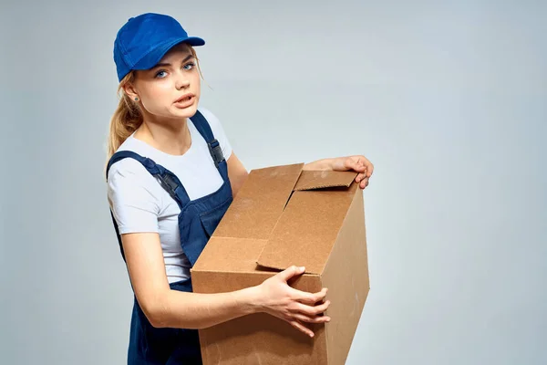 Una mujer en uniforme de trabajo con una caja en las manos de un servicio de entrega de fondo ligero —  Fotos de Stock
