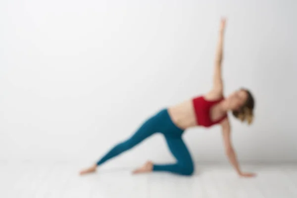 Seorang wanita dalam celana jeans biru berlatih yoga pada latar belakang cahaya dalam ruangan dan sosok ramping dalam senam — Stok Foto