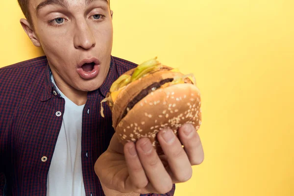 Hombre alegre con una taza de cerveza y una hamburguesa en las manos dieta estilo de vida amarillo fondo — Foto de Stock
