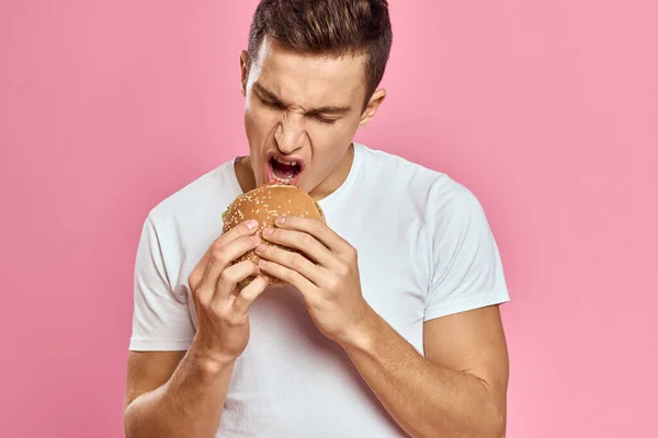 분홍색 배경의 햄버거를 먹고 있는 남자, 패스트 푸드를 먹고 있는 남자, 카피 스페이스의 근접 사진 촬영 — 스톡 사진