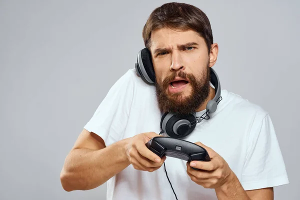 Mann mit Gamepad-Kopfhörer spielt Freizeittechnik weißes T-Shirt heller Hintergrund — Stockfoto