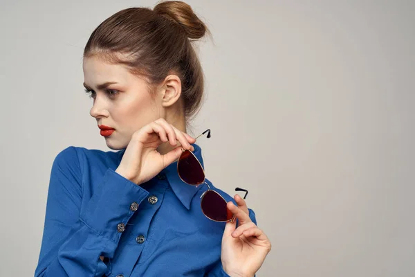 Fashionable woman in sunglasses and a blue shirt gesturing with her hands on a light background cropped view — Stock Photo, Image