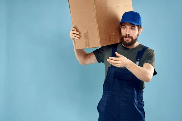 마차 배달부의 손에 상자를 들고 파란색 배경을 가진 작업복을 입고 일하고 있는 남자 — 스톡 사진