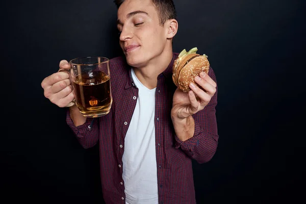 손에는 맥주 머그와 햄버거를 든 남자 재미있는 라이프 스타일 스튜디오 어둠의 고립 된 배경 — 스톡 사진