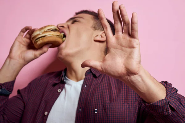 Πεινασμένος άνθρωπος με χάμπουργκερ στα χέρια fast food διατροφή συναισθήματα τροφίμων ροζ φόντο — Φωτογραφία Αρχείου