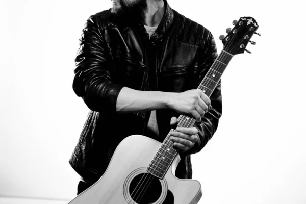 Un uomo tiene una chitarra tra le mani emozioni musicali giacca di pelle nera occhiali scuri studio sfondo chiaro — Foto Stock