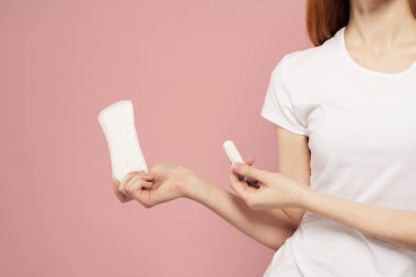 Elinde ped ve tampon olan bir kız. Pembe arka plan adet dönemi. Hijyen konusunda kritik günler.