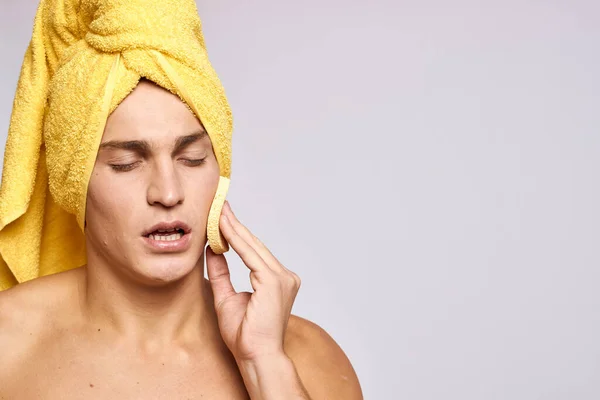 Schöner Mann mit Kosmetik-Gesichtsschwamm und gelbem Handtuch auf dem Kopf — Stockfoto